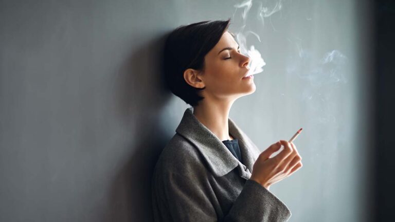 Portrait of fashionable woman smoking a cigarette on dark backgr