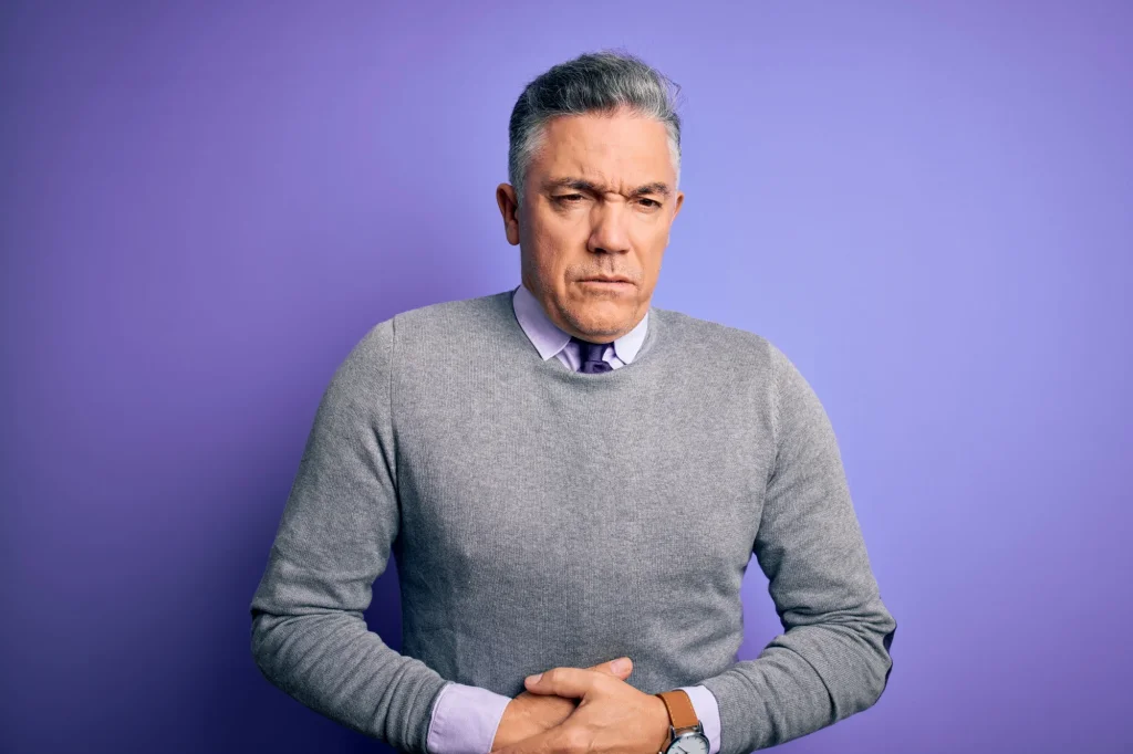 middle-age-handsome-greyhaired-man-wearing-elegant-sweater-purple-background-with-hand-stomach-because-indigestion-painful-illness-feeling-unwell-ache-concept