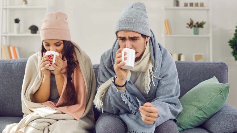 Sad,Sick,Young,Couple,Wrapped,In,Plaid,Sitting,On,Sofa