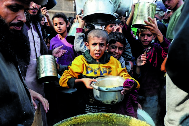 Palestinians gather to receive meals cooked by a charity kitchen, in Deir Al-Balah, central Gaza Strip