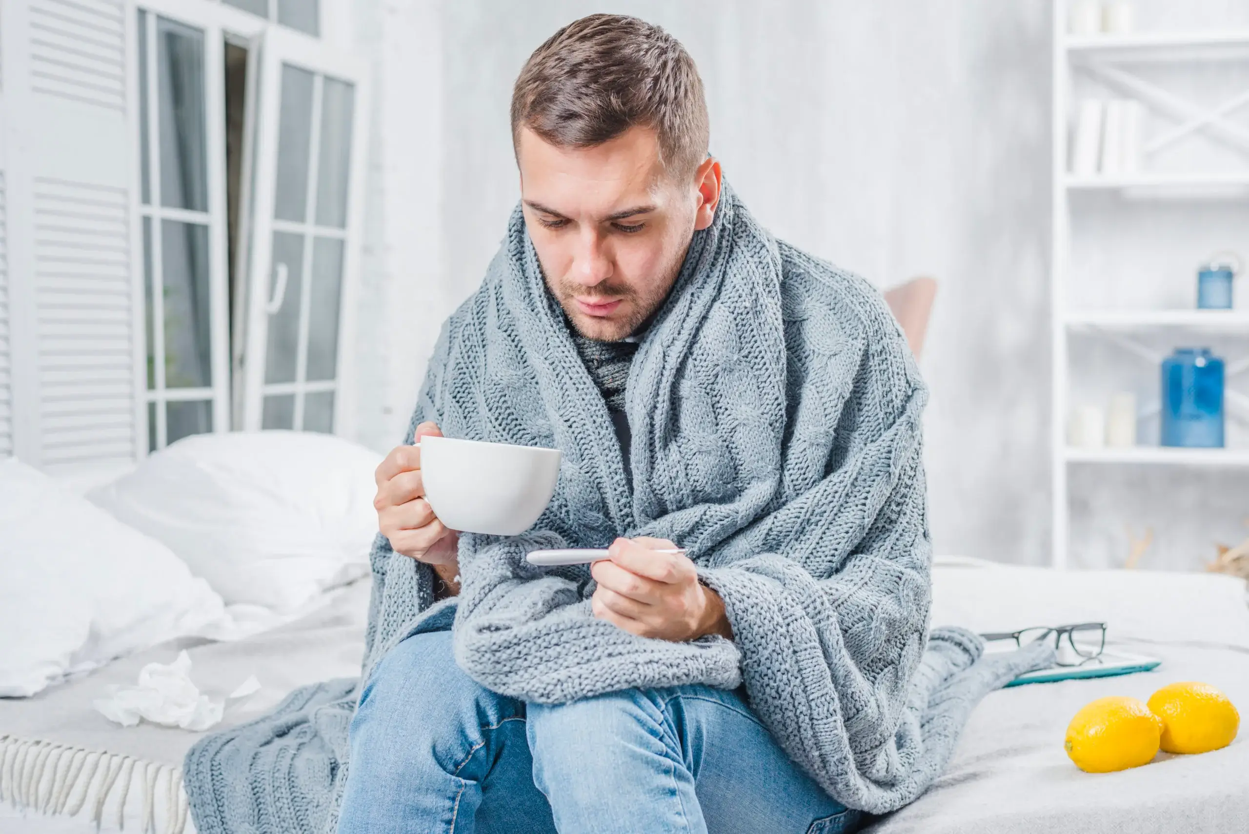 sick-man-sitting-bed-holding-cup-coffee-checking-fever-thermometer-scaled
