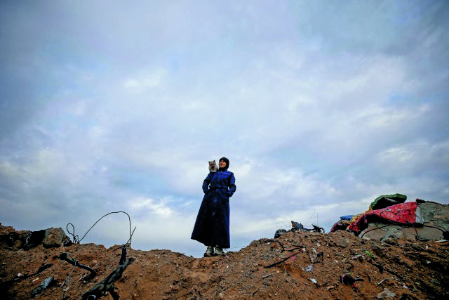 A Palestinian woman carries a cat on her shoulder as she stands near the rubble of her house, on a rainy day, amid a ceasefire between Israel and Hamas, in Jabalia refugee camp in the northern Gaza Strip