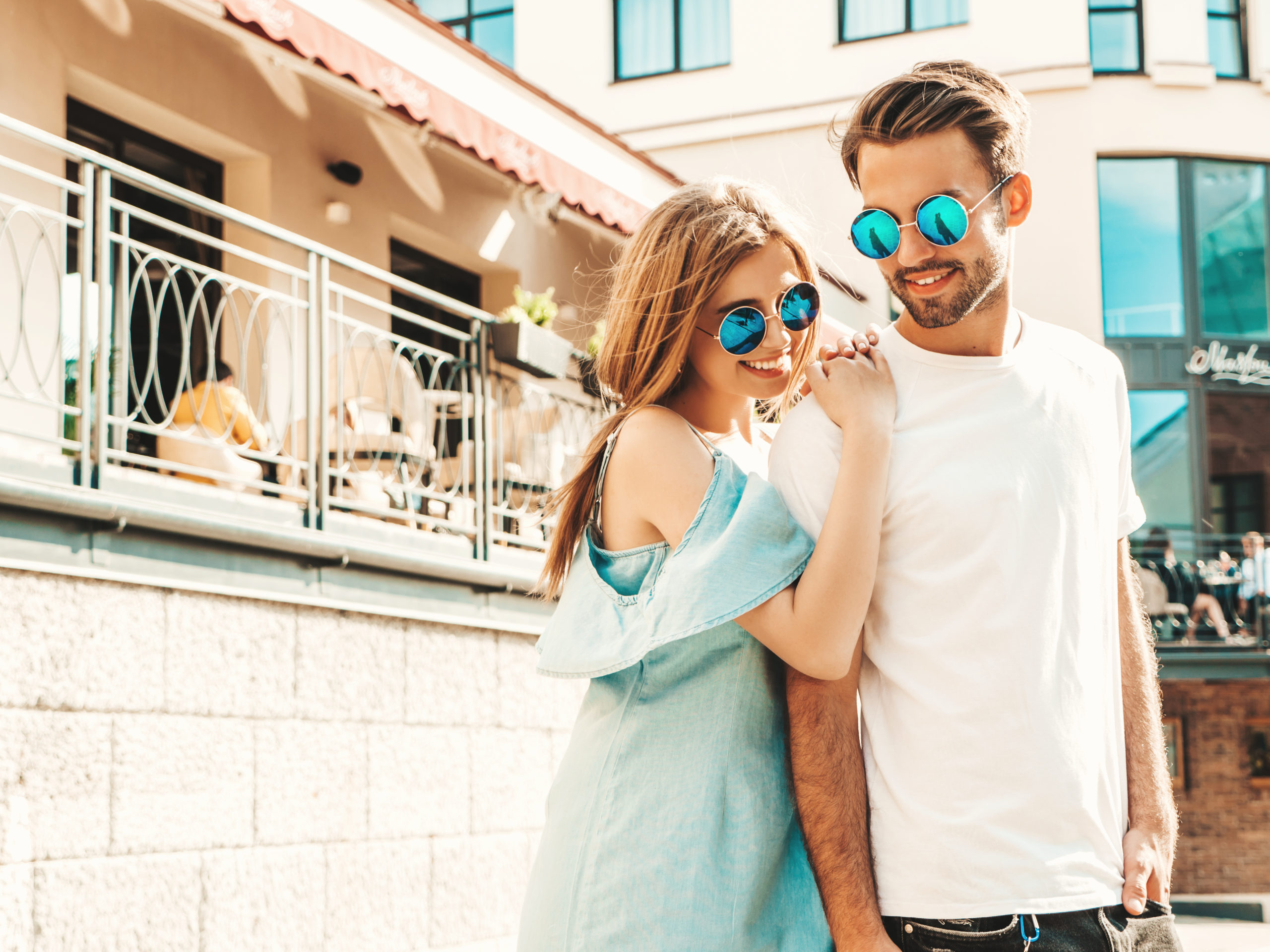 Portrait of smiling beautiful woman and her handsome boyfriend. Woman in casual summer jeans dress. Happy cheerful family. Female having fun. Couple posing on the street background in sunglasses